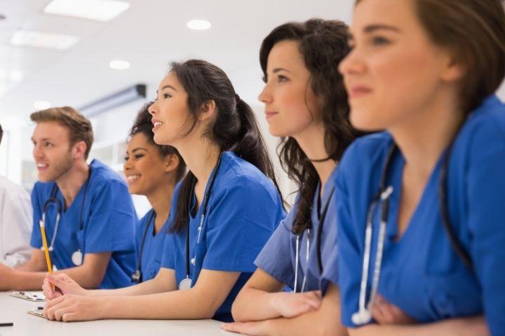 Five students wear scrubs and train for a medical career.