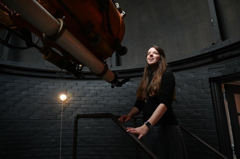 Student standing in front of a telescope