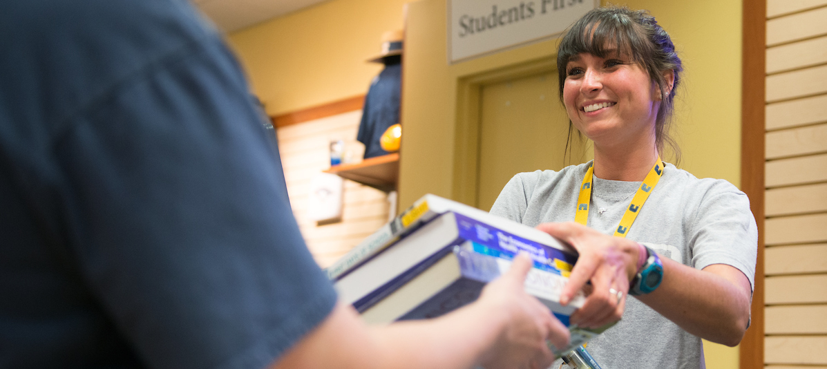 Girl handing books to student at bookstore