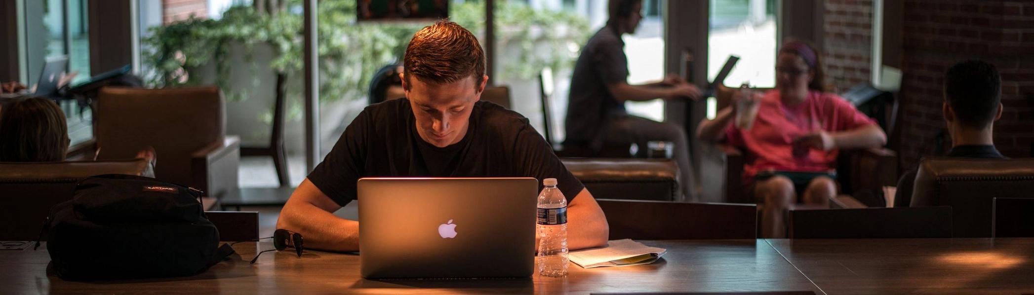 UTC student working on his laptop in a cafe with other patrons.