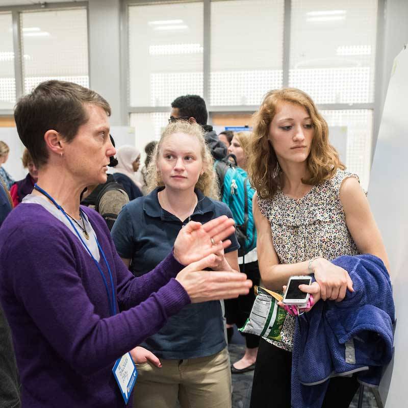 female professor talks to female students standing in front of research poster