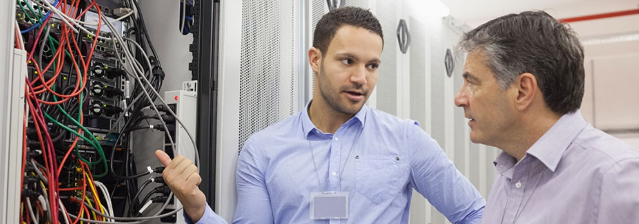 CISA Website Banner A male systems auditor inspecting a network while talking to an older male.