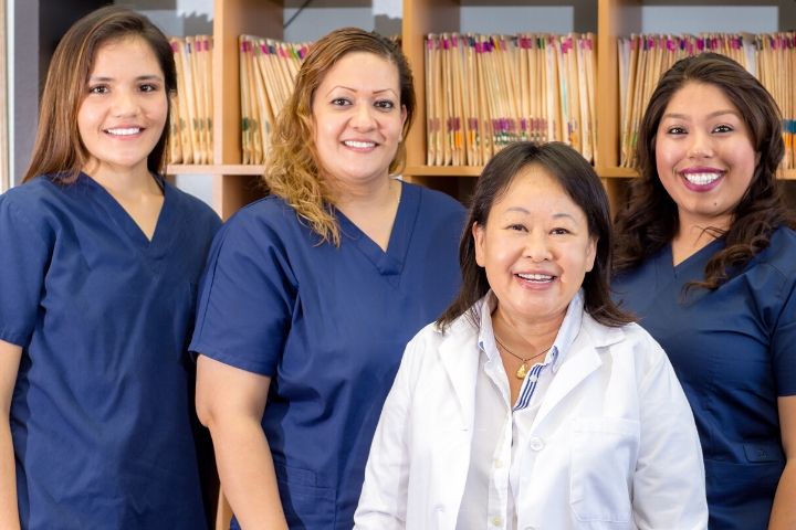 Medical billing and coding students in scrubs stand together in front of files.