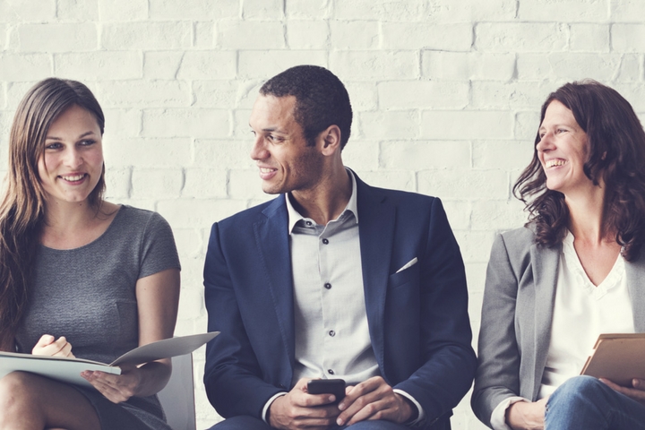 Three people holding books and folders and smiling at each other