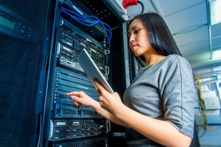 A woman standing at a computer system holding a tablet