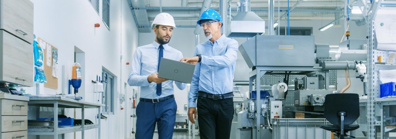 Two men wearing hard hats walking through a factory and tlaking