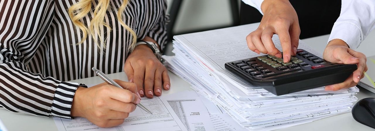 A man and a woman looking at a calculator and writing down the calculations