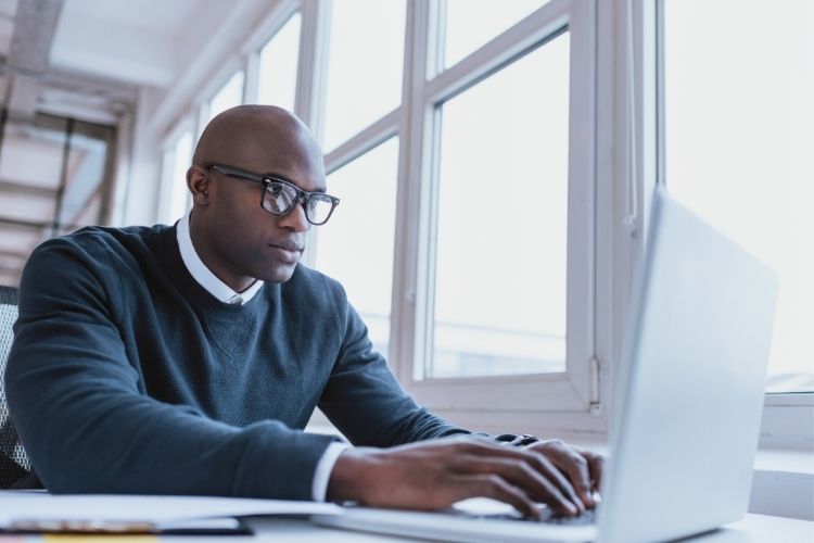 A man sitting at a desk typing on a laptop.