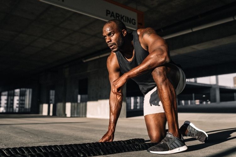 A man who is in workout attire kneeling about to exercise with weighted ropes.