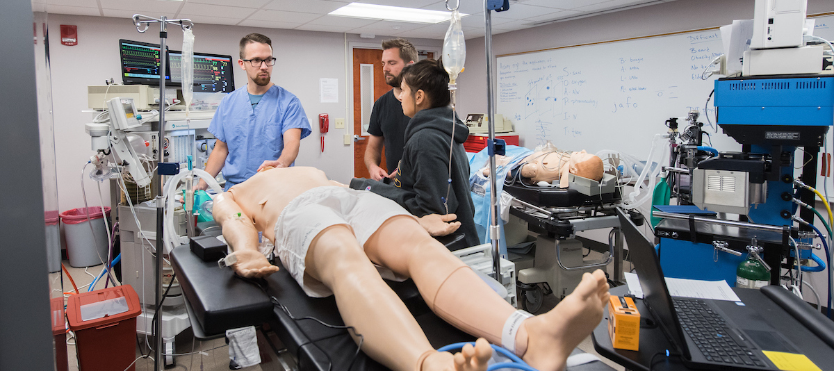 Nurse Anesthesia sim lab 3 2 men and 1 woman standing around a dummy