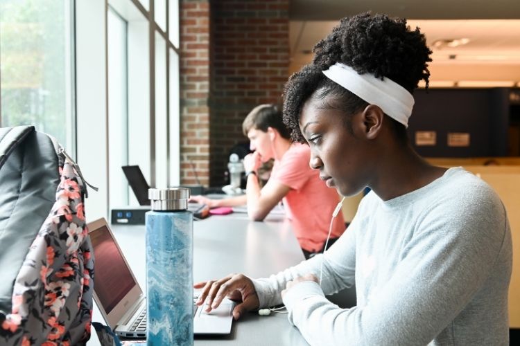 A student sitting in the UTC Library scrolling on her laptop