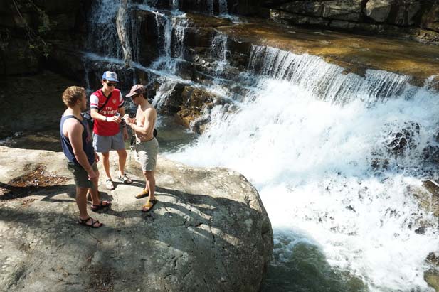 group of three standing by waterfall