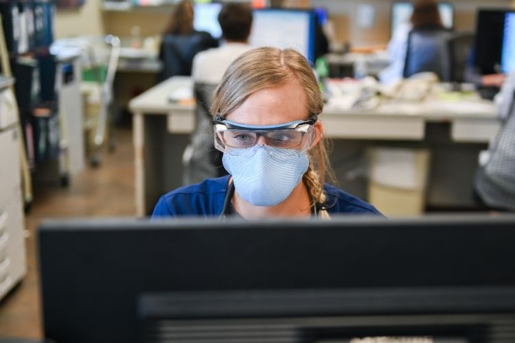 A nurse wearking PPE while working on a computer