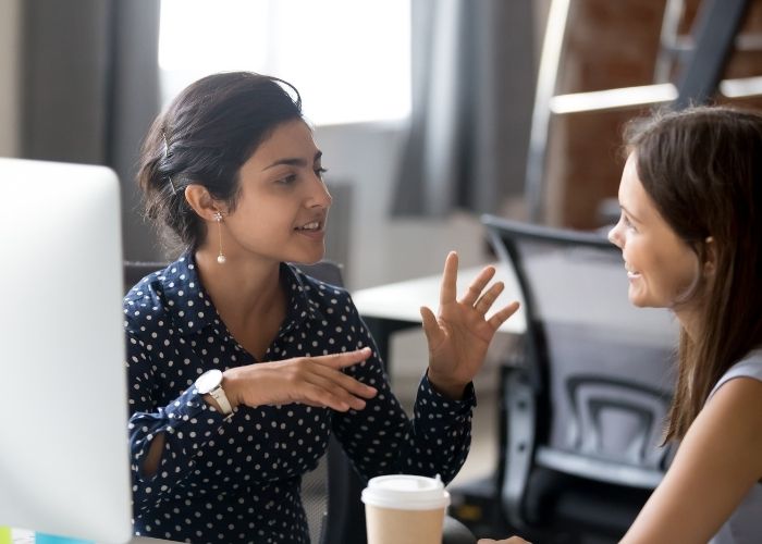 Two colleagues chatting while sitting near laptops