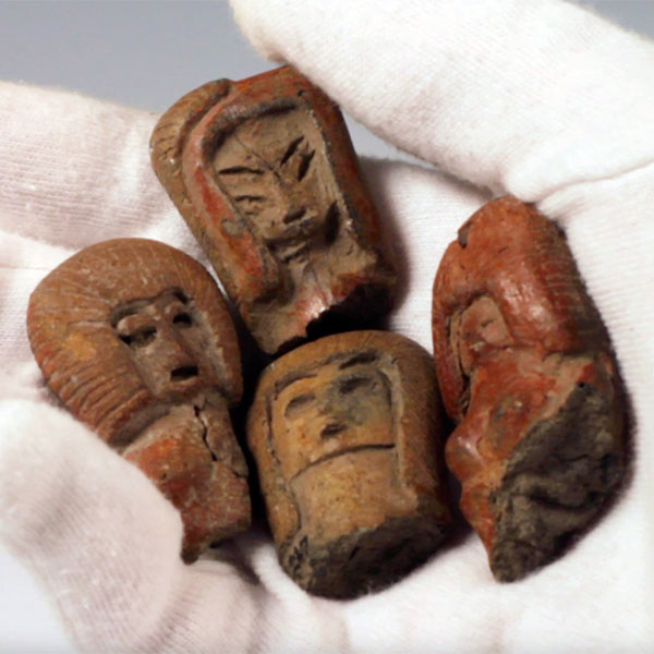 Four pre-Columbian ceramic figurine heads made from a red clay.