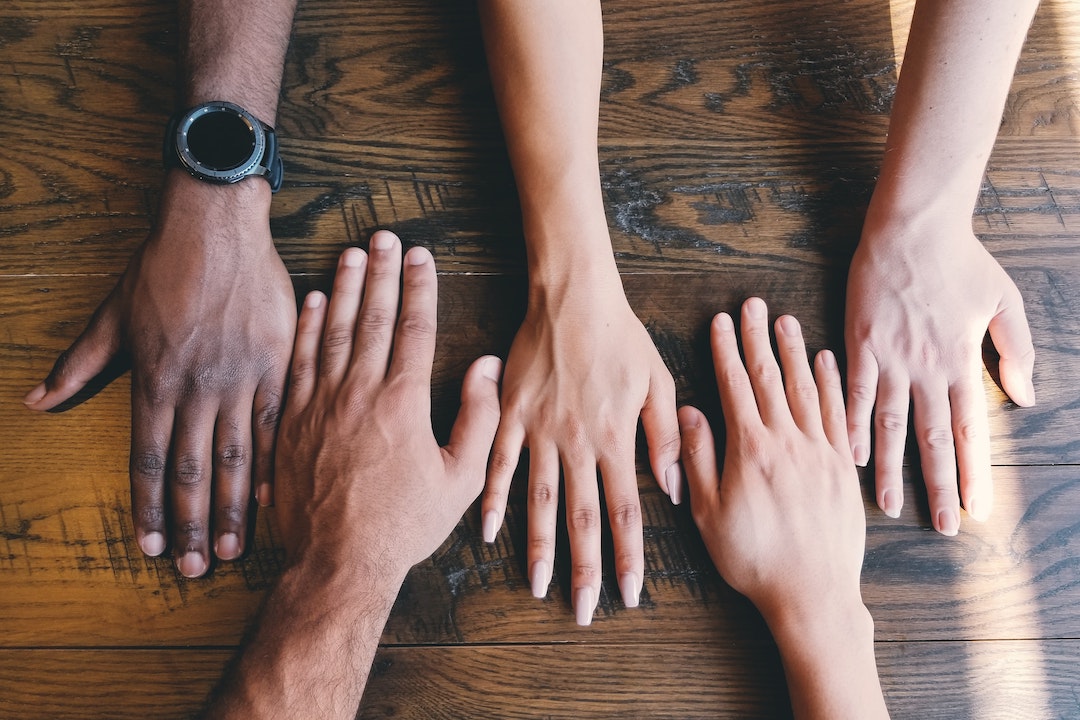 hands of different skin colors lined up together on a wooden table