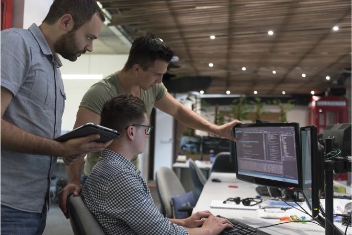 A group of software developers looking at a computer screen discussing an issue.