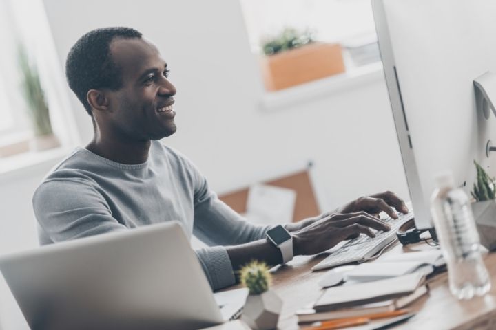 A man sitting at a desk smiling while he types on a keyboard