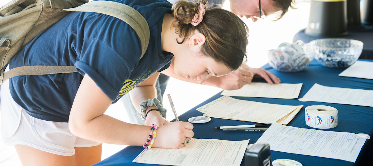 female student standing at desk signing up to vote