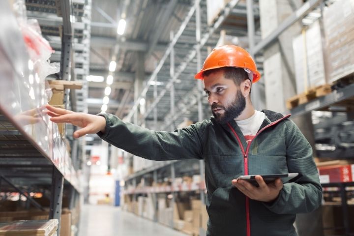 A warehouse manager checking the stock of a warehouse while holding an iPad.