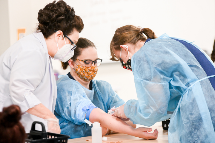 Phlebotomy Technician students practicing their phlebotomy skills while the instructor supervises