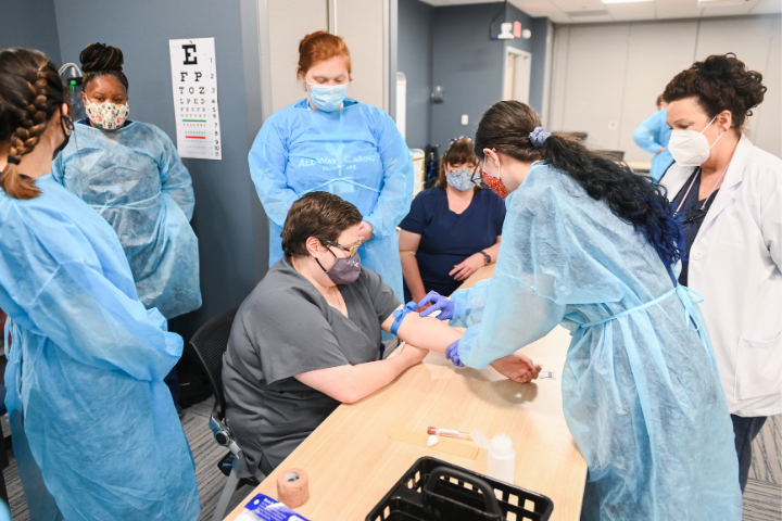 A phlebotomy technician student practicing her skills while other students observe