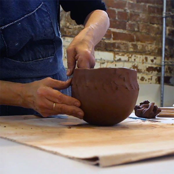 Potter uses fingers to pinch coil to red clay base