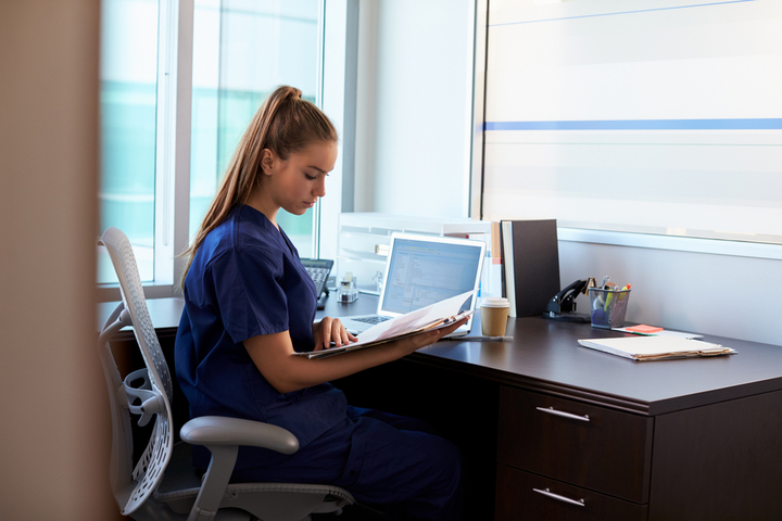 Medical billing and coding specialist sits at desk with files and a laptop.