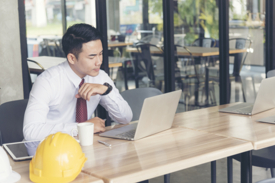 male looking at laptop with hard hat on desk next to him