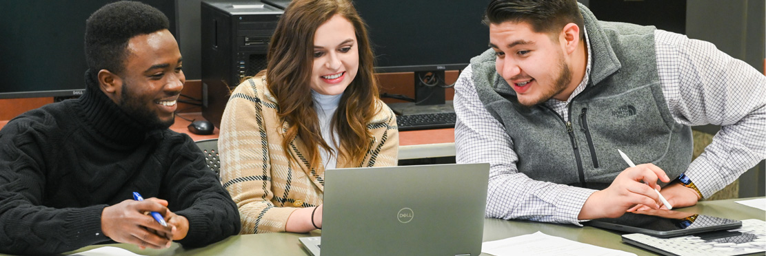 A photo of three students at a workstation discussing a project.