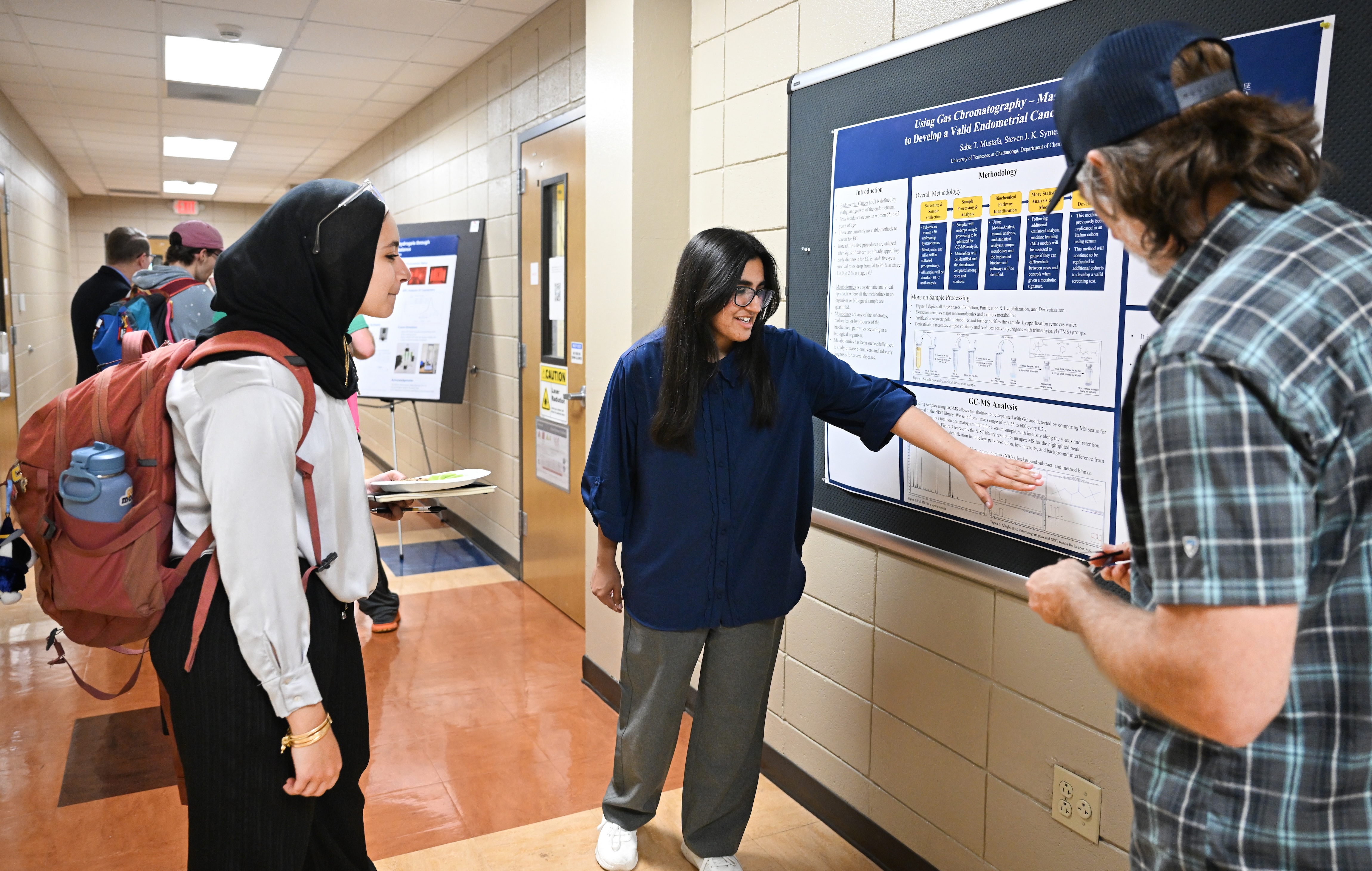 Students review poster presentations in hallway. 