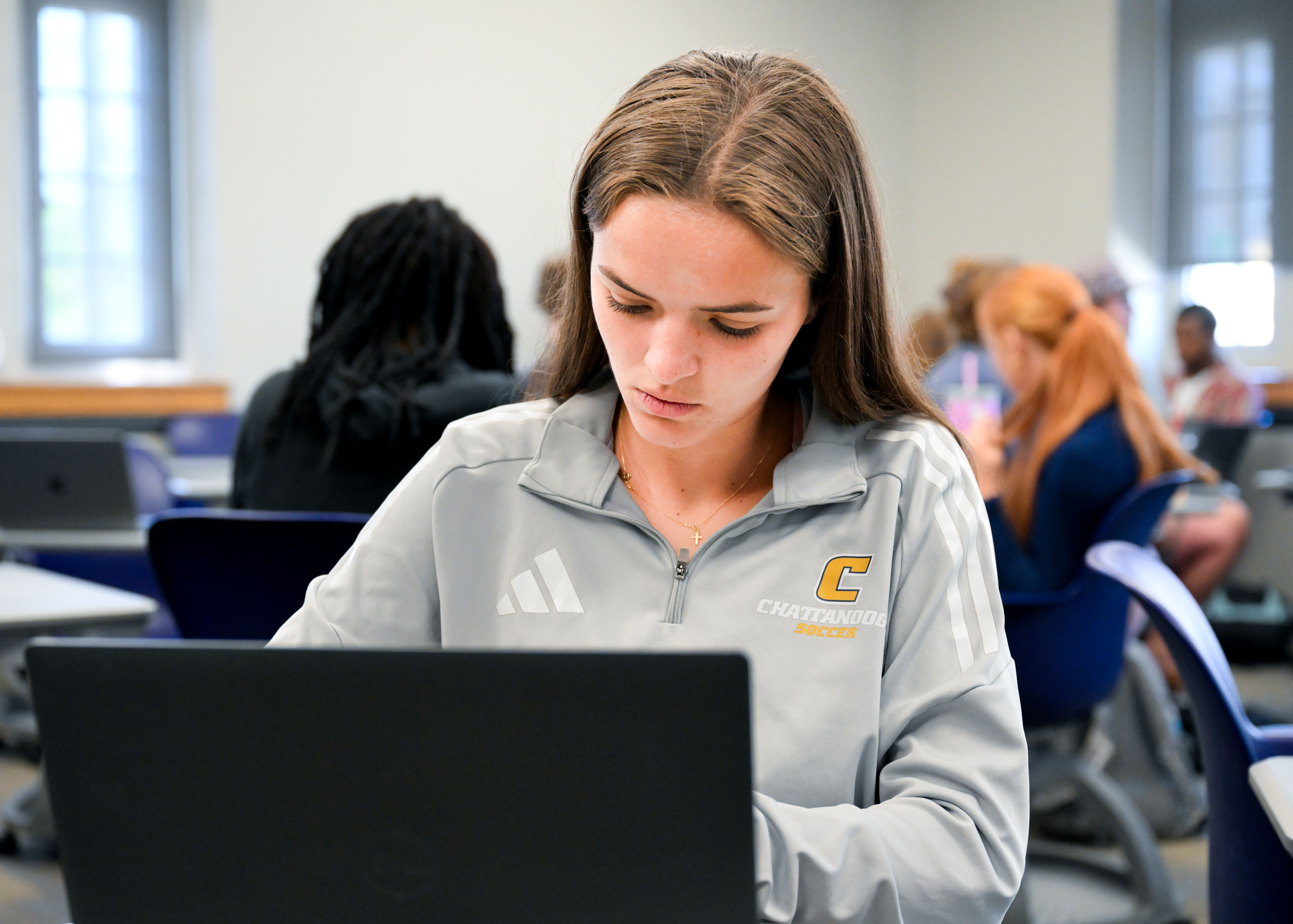 RCOB student working in a classroom with a laptop in front of her and other students behind her. 