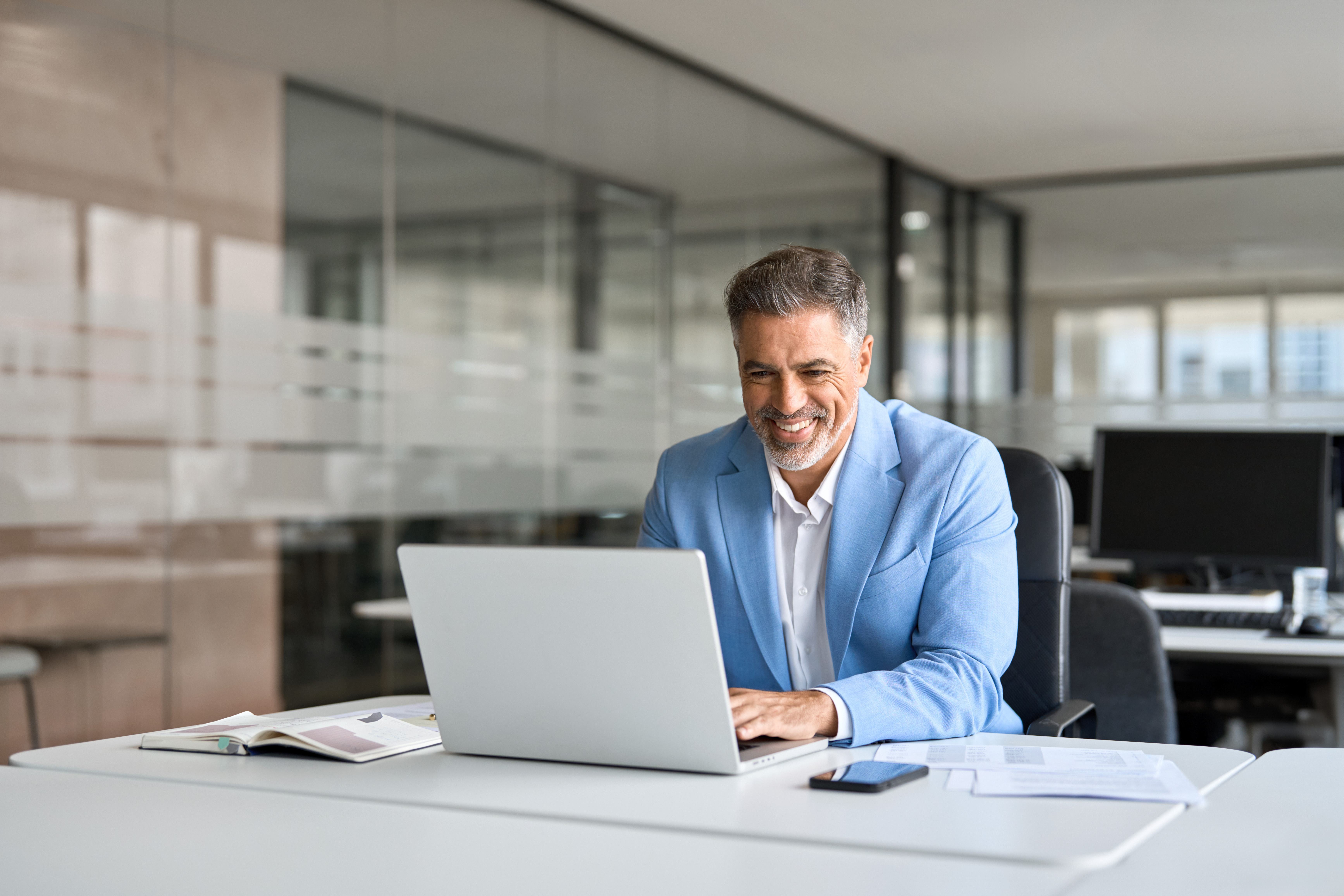 Mature professional man learns to use AI at work, smiling at computer