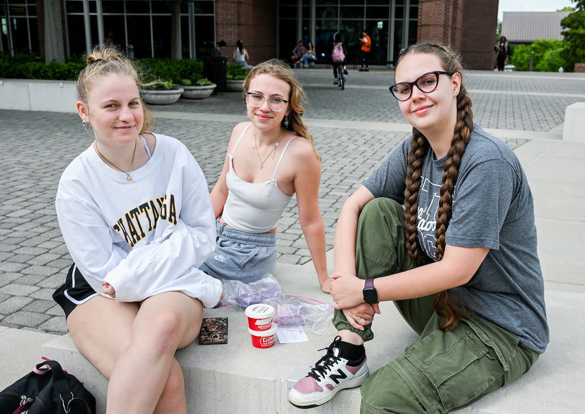 Three students sitting on a knee wall outside of the library