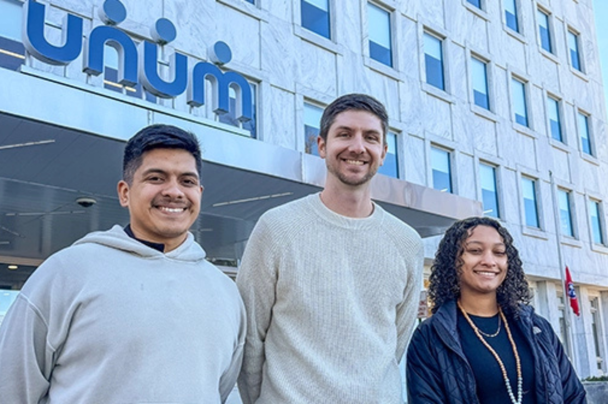 Two Unum scholars and a Unum representative stand outside of the Unum headquarters in Chattanooga.