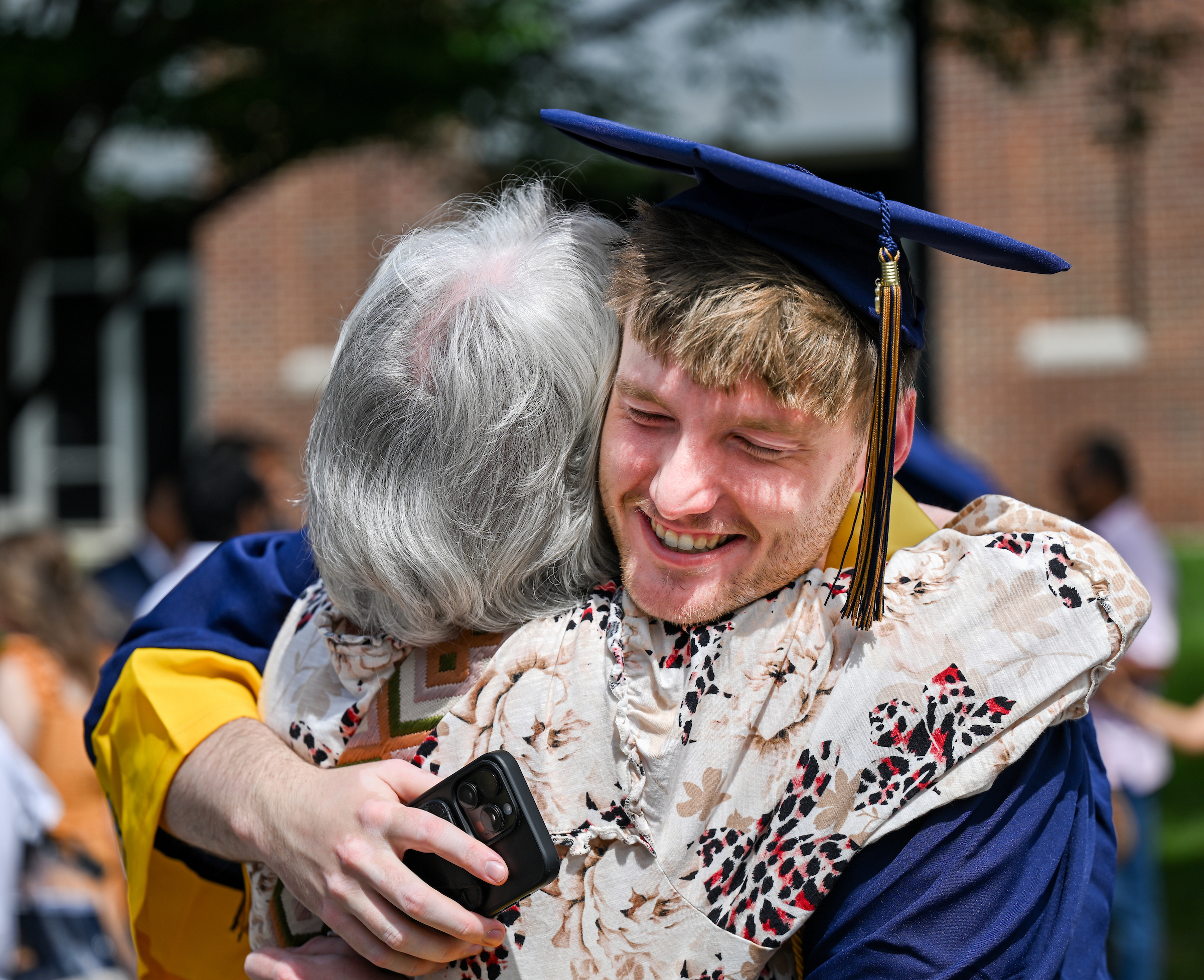 UTC graduate smiles as he hugs a woman after commencement. 