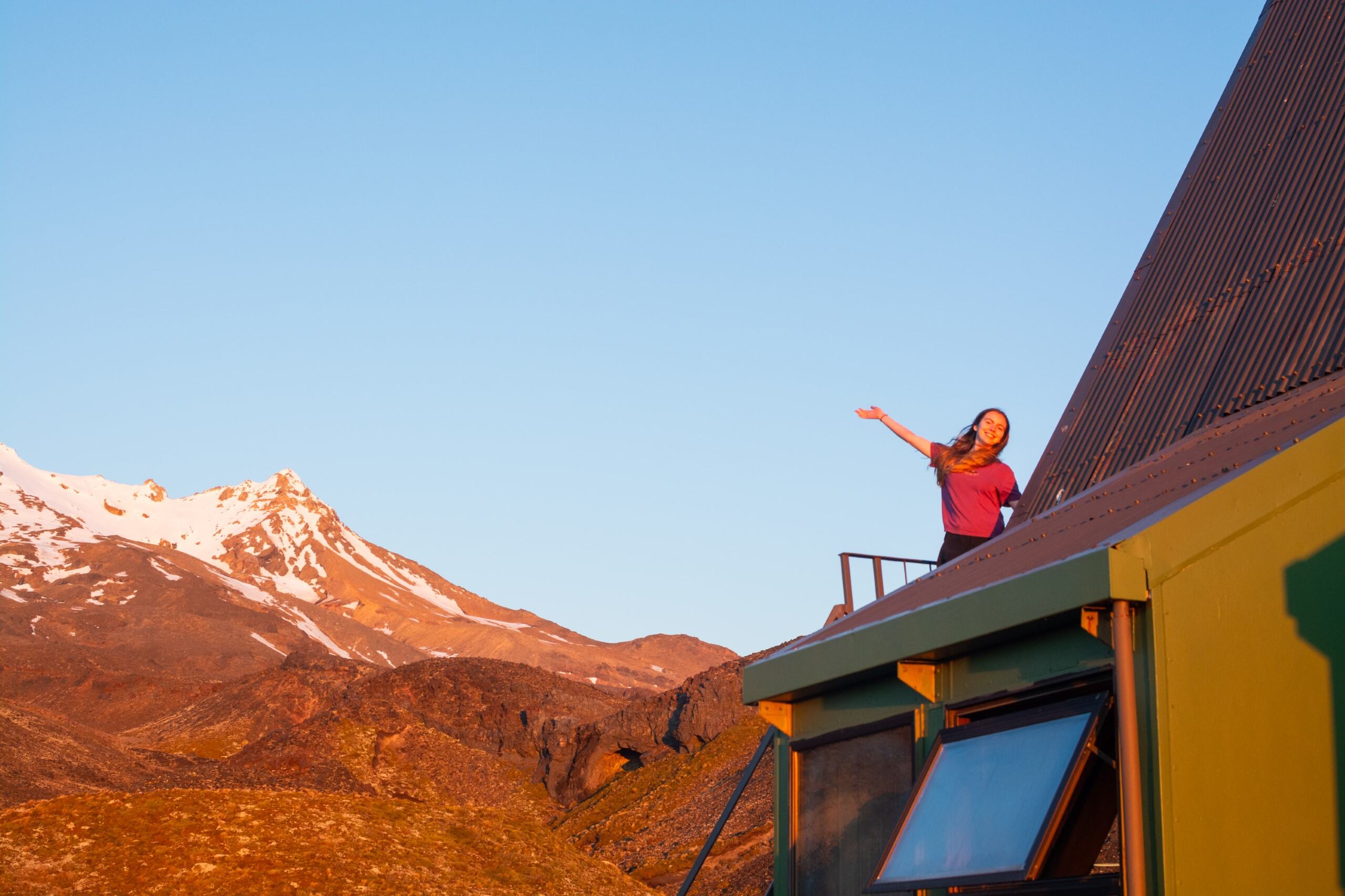 Woman waving from cabin roof near snow-capped mountain, New Zealand