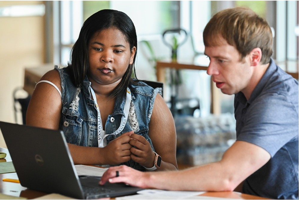 An academic advisor helping a student register for classes on a computer.