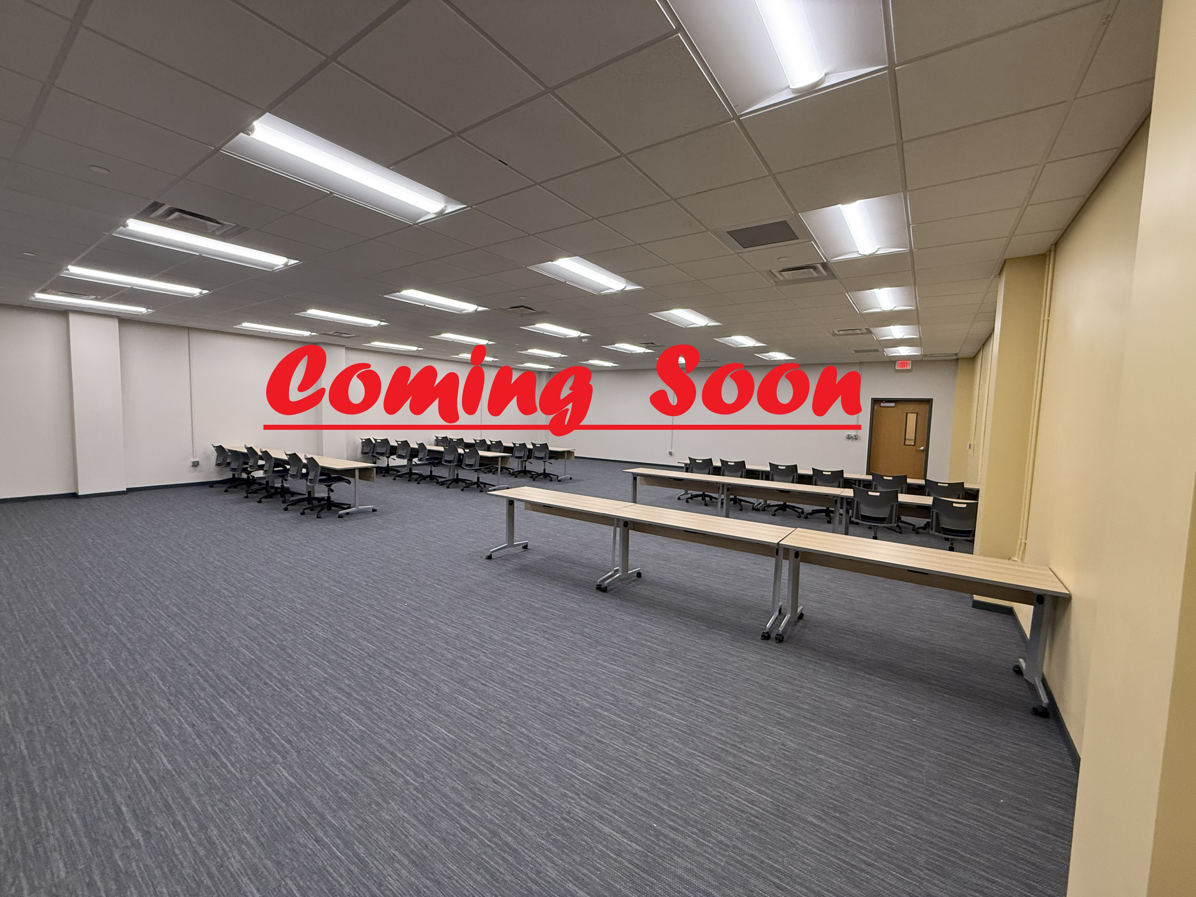 Picture of room 320 in the University Center. There are tables and chairs in the space facing the front of the room. The words "Coming Soon" have been added to the picture. 