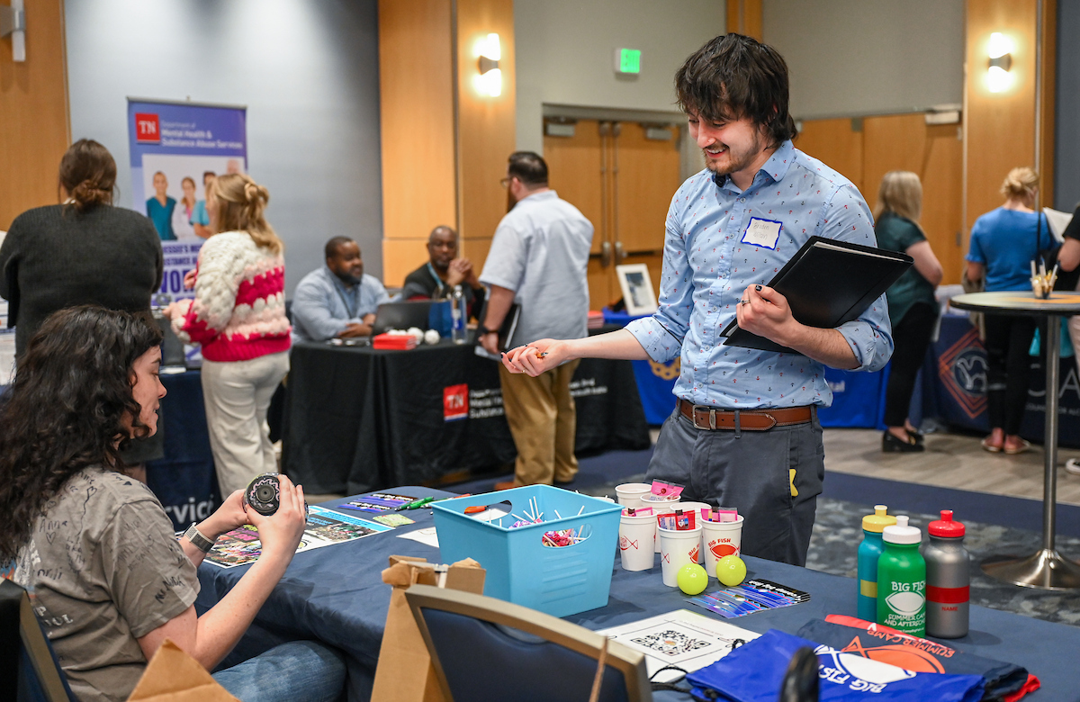 UTC student standing at a table holding a folio at the Social Work Career fair talking with a representative