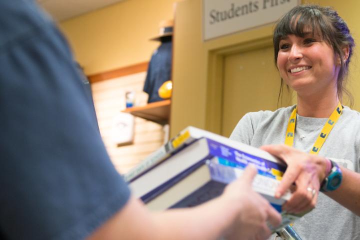 Girl handing books to student at bookstore