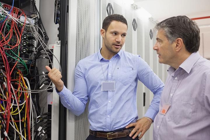 A male auditor talking with an individual while reviewing a system