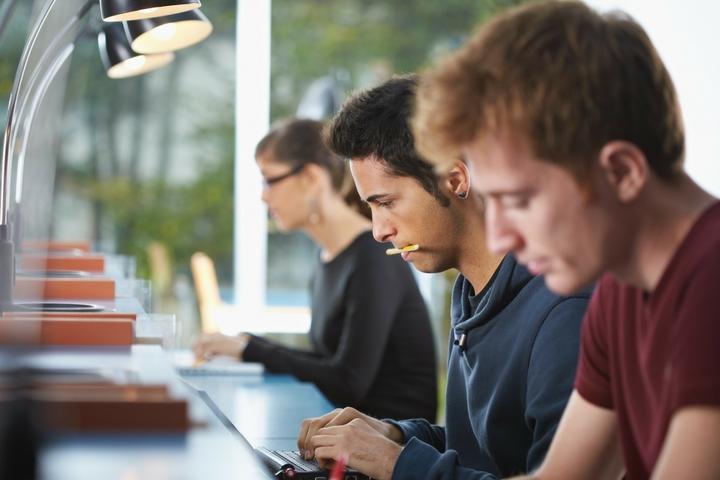 three people studying their own things and sitting at a long table