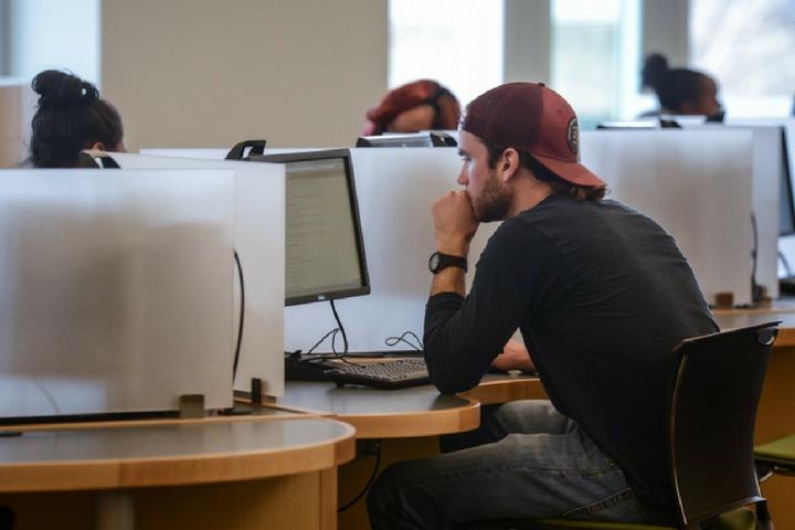 Students sitting at computers with dividers in the library