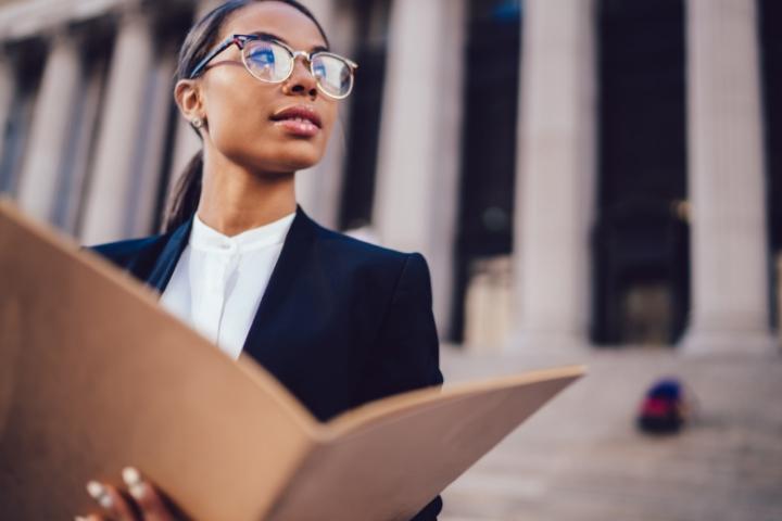 A female paralegal standing outside of a courthouse holding a file folder