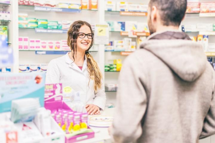 Women behind pharmacy counter talking to male customer
