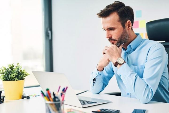 A man sitting at desk looking at a laptop