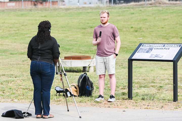 Student records a video by a sign with a microphone 