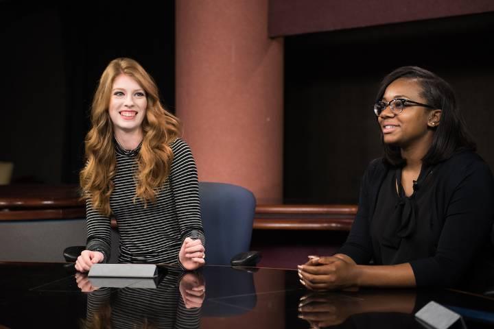 Two students sit in newsroom setting