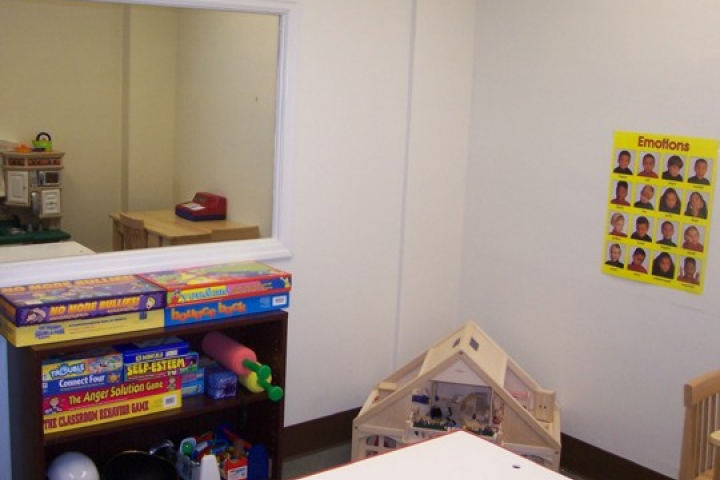 image of playroom for play therapy with doll house, shelf with games